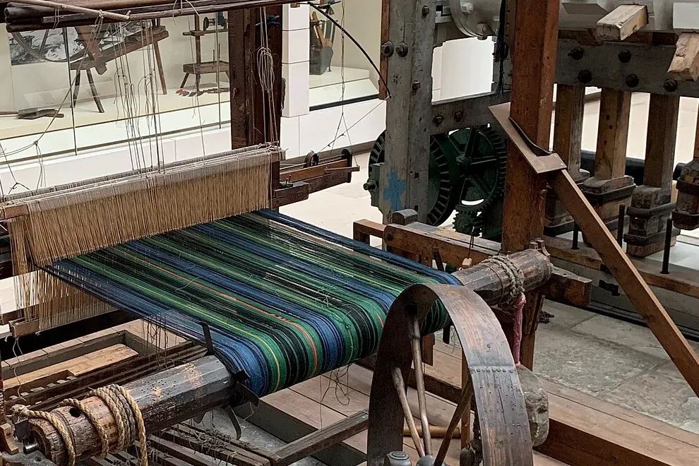 Alat tenun kayu berpedal dengan kain bergaris hijau dan biru di atasnya